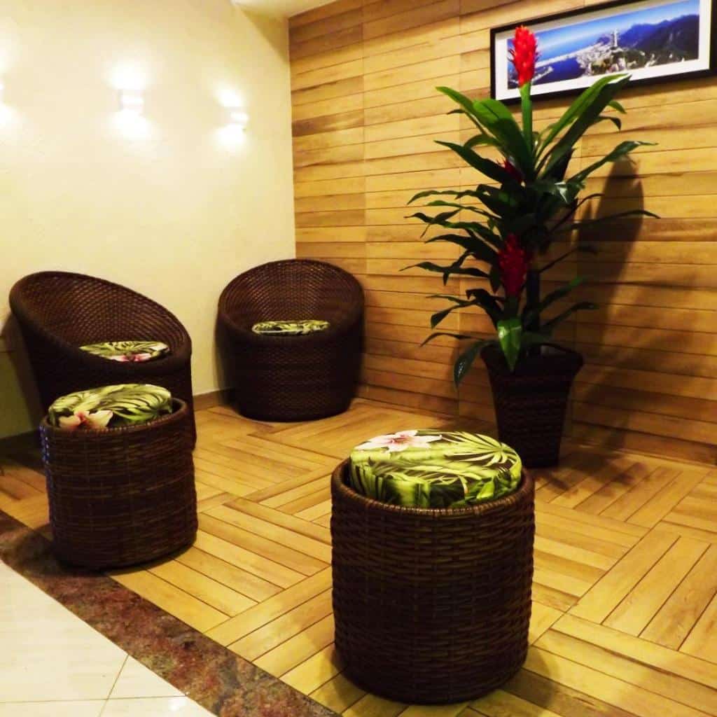 Área de estar aconchegante com cadeiras de vime, almofadas tropicais e arte em painéis de madeira no Downtown Santana Hotel.