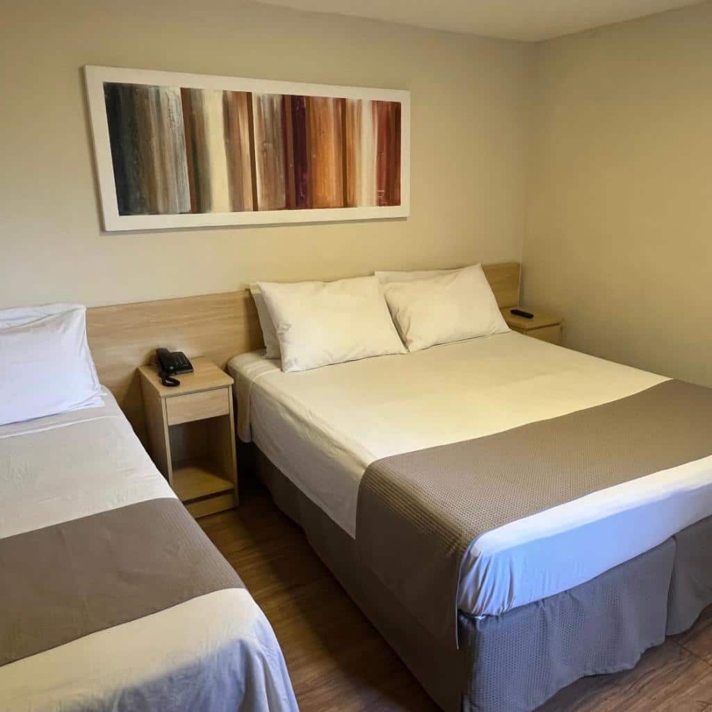 Um quarto do Hotel Galícia com duas camas, roupa de cama neutra, piso de madeira e arte abstrata na parede.