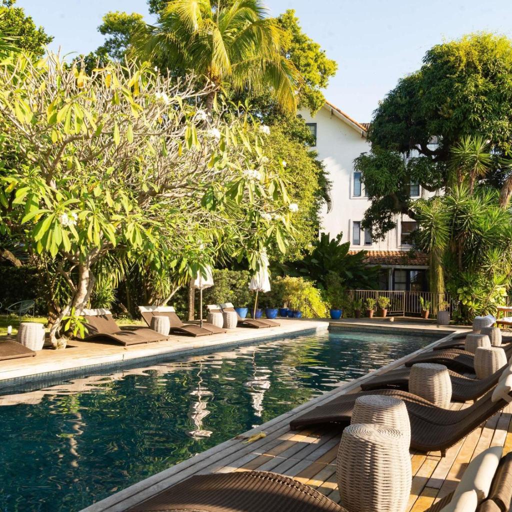 Piscina externa com espreguiçadeiras, guarda-sóis e árvores exuberantes no Santa Teresa Hotel Rio de Janeiro - MGallery Collection.
